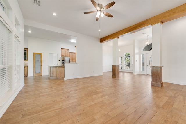 unfurnished living room featuring beam ceiling, sink, a high ceiling, light hardwood / wood-style floors, and ceiling fan with notable chandelier