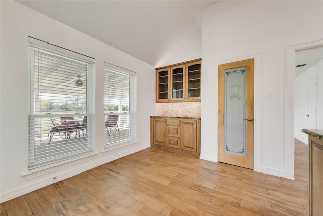 kitchen featuring lofted ceiling, light wood-type flooring, backsplash, and stone counters