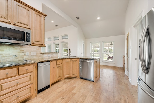 kitchen with sink, light stone countertops, light wood-type flooring, light brown cabinetry, and appliances with stainless steel finishes