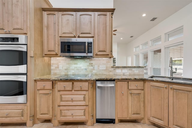 kitchen with light stone countertops, appliances with stainless steel finishes, decorative backsplash, light brown cabinetry, and sink