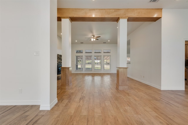 unfurnished living room featuring ceiling fan, beam ceiling, a stone fireplace, and light wood-type flooring