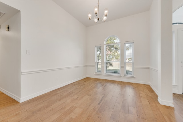 empty room with light wood-type flooring, high vaulted ceiling, and a notable chandelier