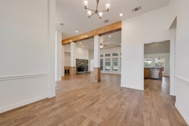 unfurnished living room featuring ceiling fan with notable chandelier, beam ceiling, a stone fireplace, and light hardwood / wood-style flooring