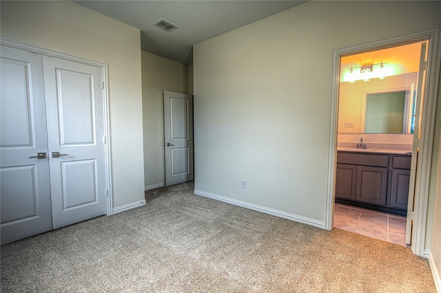 unfurnished bedroom featuring sink, light colored carpet, a closet, and ensuite bathroom