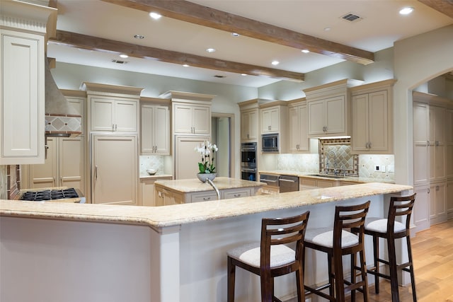 kitchen featuring decorative backsplash, light stone counters, beamed ceiling, light hardwood / wood-style floors, and a kitchen island