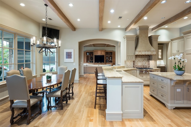 kitchen with premium range hood, beam ceiling, light hardwood / wood-style floors, and decorative light fixtures