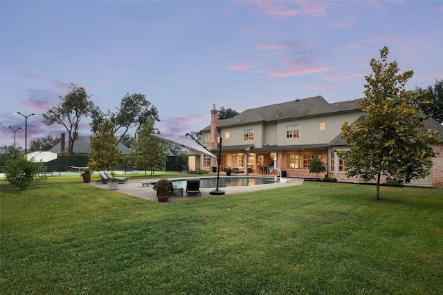 back house at dusk featuring a lawn and a patio area