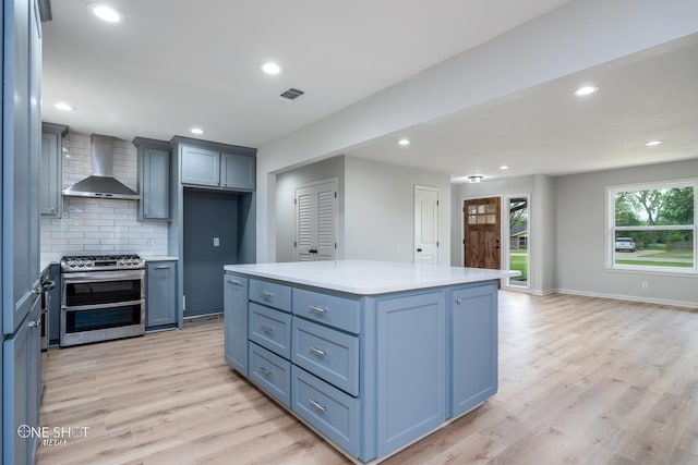 kitchen featuring double oven range, backsplash, wall chimney range hood, light hardwood / wood-style flooring, and a kitchen island