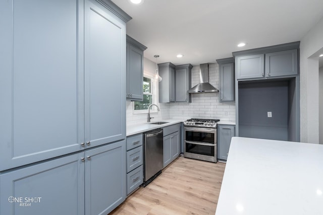 kitchen featuring pendant lighting, sink, light hardwood / wood-style flooring, wall chimney exhaust hood, and appliances with stainless steel finishes