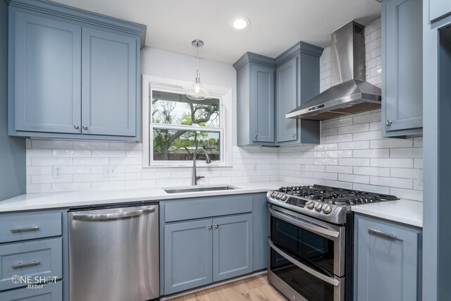 kitchen with light wood-type flooring, tasteful backsplash, stainless steel appliances, sink, and wall chimney range hood