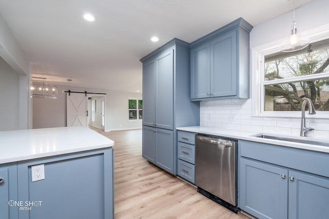 kitchen featuring dishwasher, backsplash, sink, a barn door, and light hardwood / wood-style floors