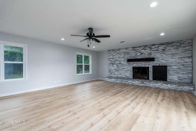 unfurnished living room with ceiling fan, a stone fireplace, and light wood-type flooring