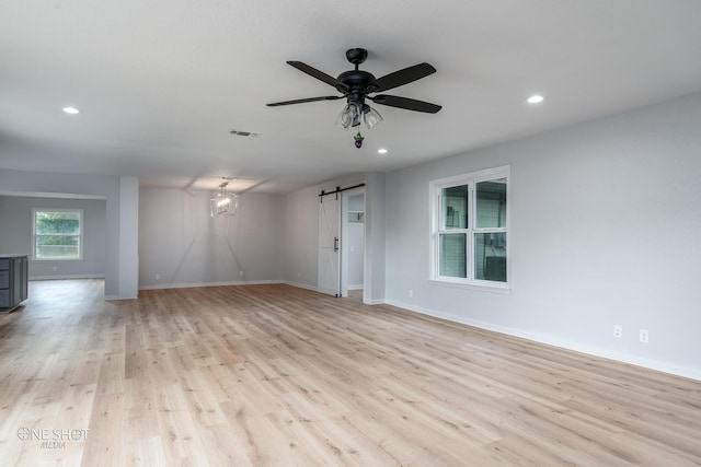 unfurnished room with a barn door, ceiling fan, and light wood-type flooring