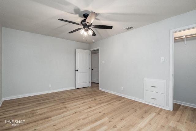 unfurnished bedroom with a walk in closet, light wood-type flooring, a closet, and ceiling fan