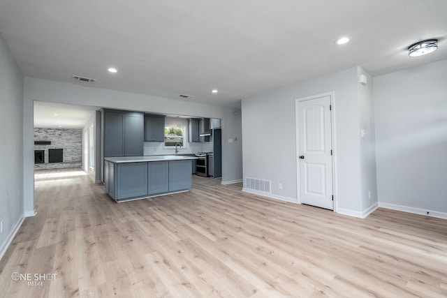 kitchen with gray cabinets, light hardwood / wood-style floors, stainless steel stove, and a large fireplace