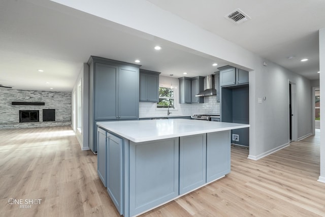 kitchen featuring gray cabinets, a center island, wall chimney range hood, and light wood-type flooring