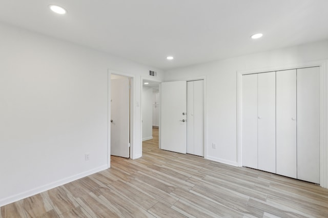 unfurnished bedroom featuring light wood-type flooring and two closets