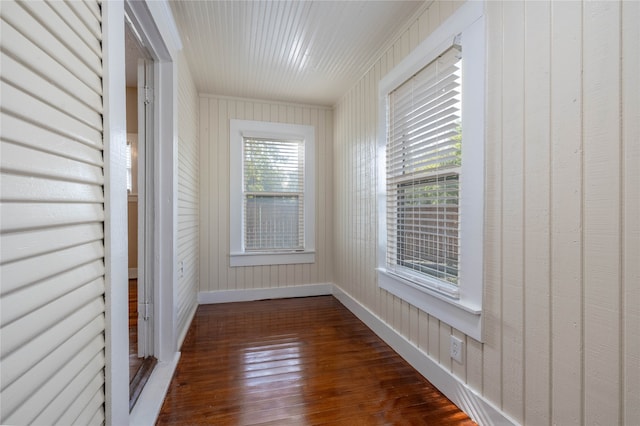 empty room with a wealth of natural light, wooden walls, and dark wood-type flooring