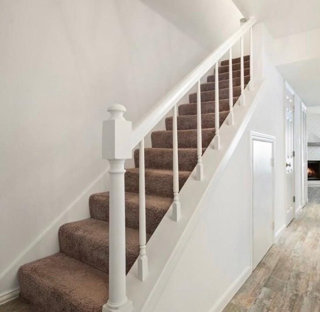 stairway featuring a warm lit fireplace and wood finished floors