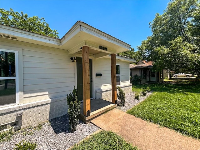 doorway to property with a lawn and brick siding