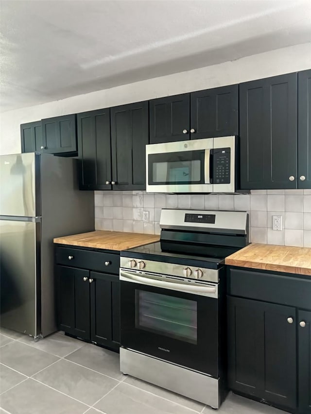 kitchen featuring light tile patterned floors, tasteful backsplash, appliances with stainless steel finishes, and butcher block counters