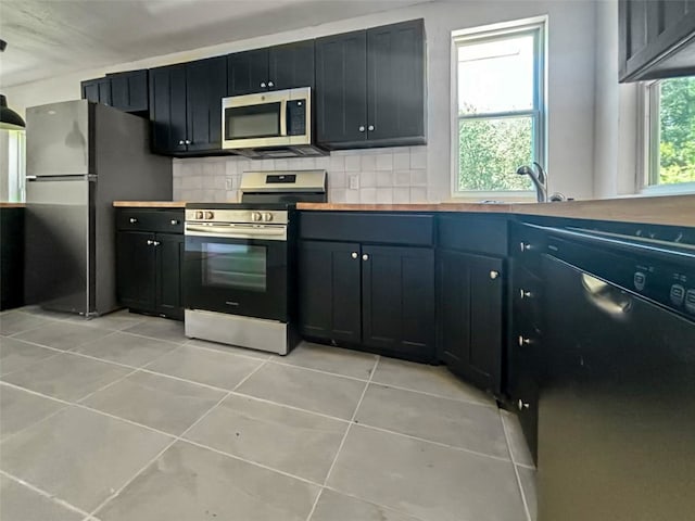 kitchen with light tile patterned flooring, a sink, butcher block countertops, stainless steel appliances, and backsplash