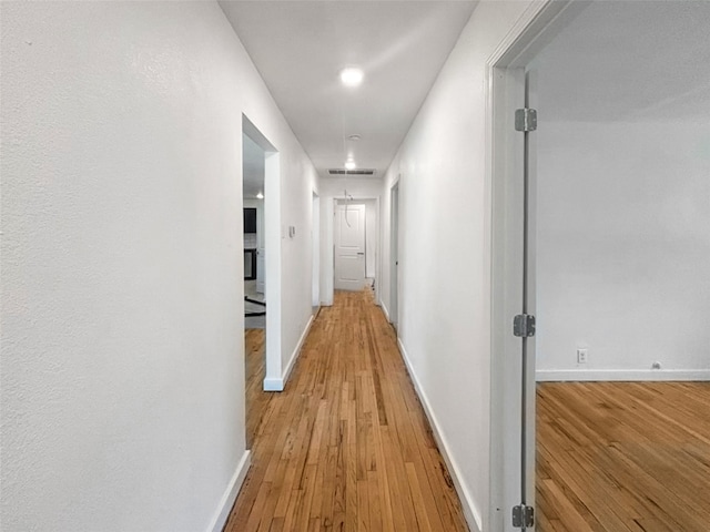 corridor featuring visible vents, light wood-style flooring, attic access, and baseboards