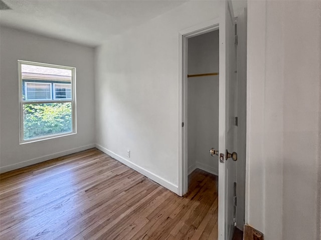 unfurnished bedroom featuring a closet, baseboards, wood finished floors, and a spacious closet