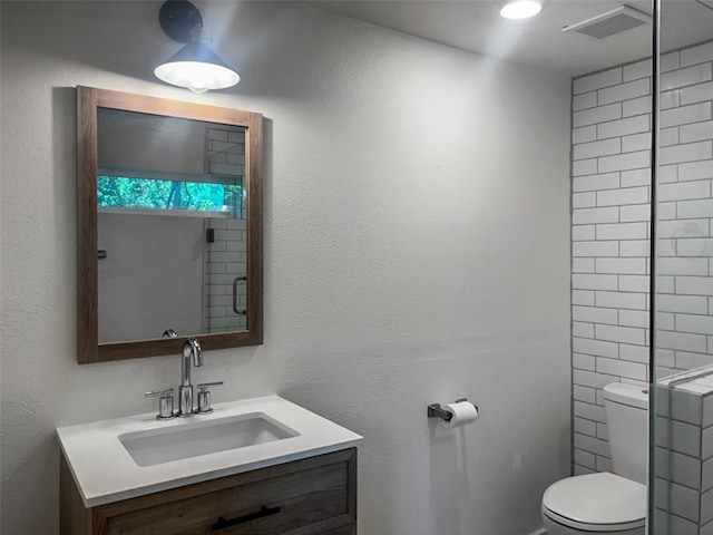 full bathroom featuring vanity, toilet, a textured wall, and visible vents