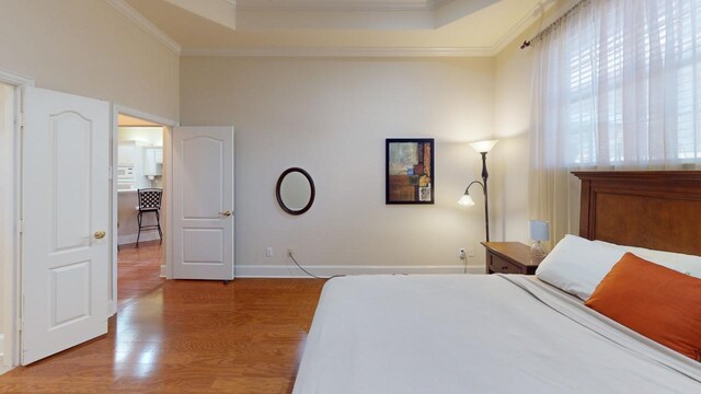 bedroom with light wood-type flooring, crown molding, and a tray ceiling