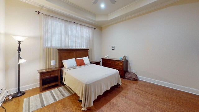 bedroom with hardwood / wood-style flooring, ceiling fan, crown molding, and a tray ceiling