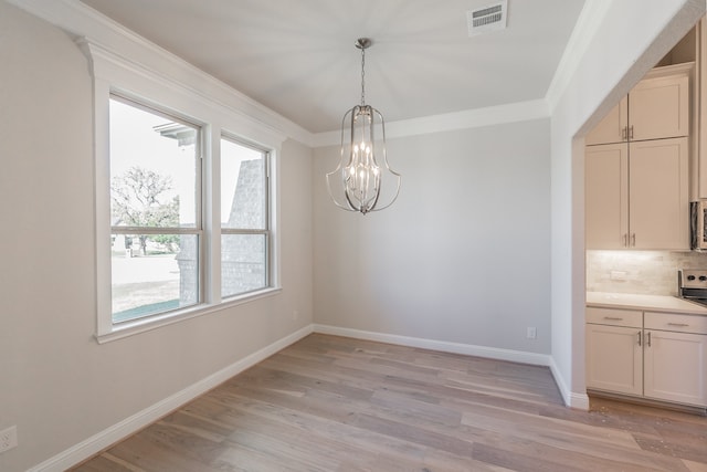 unfurnished dining area with an inviting chandelier, crown molding, and light hardwood / wood-style flooring