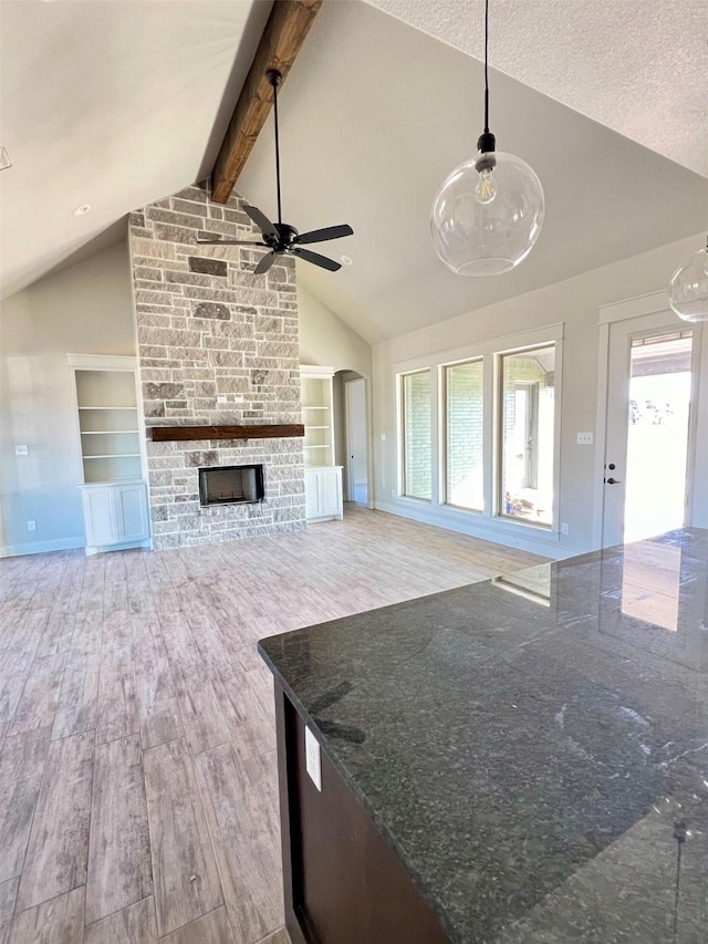 unfurnished living room with vaulted ceiling with beams, ceiling fan, a fireplace, hardwood / wood-style flooring, and built in shelves