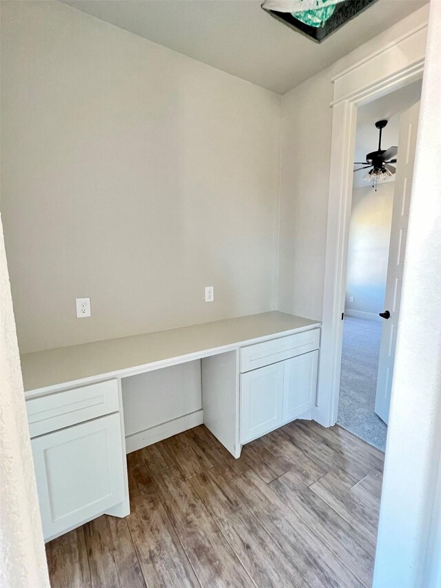 unfurnished office with light wood-type flooring, ceiling fan, and built in desk