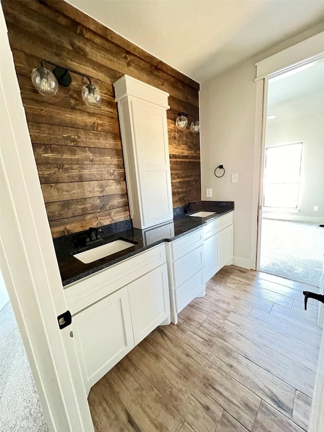 bar with sink, light wood-type flooring, wood walls, and white cabinetry