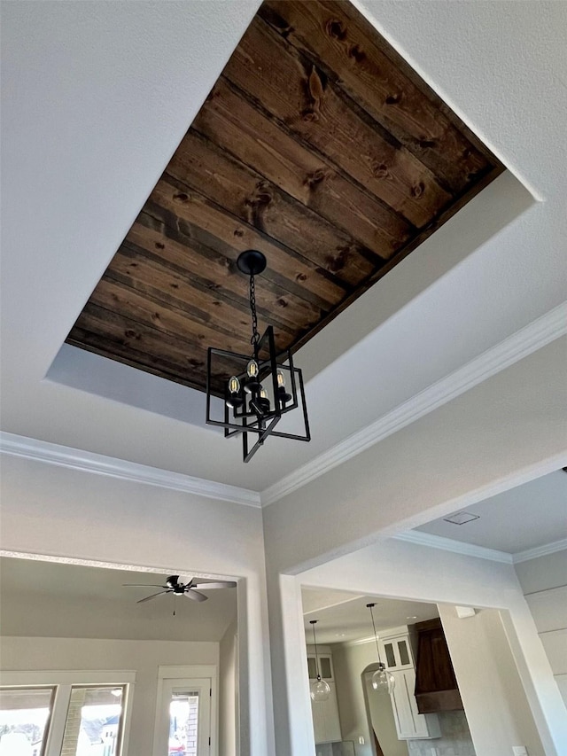 room details with wooden ceiling, crown molding, ceiling fan with notable chandelier, and a tray ceiling