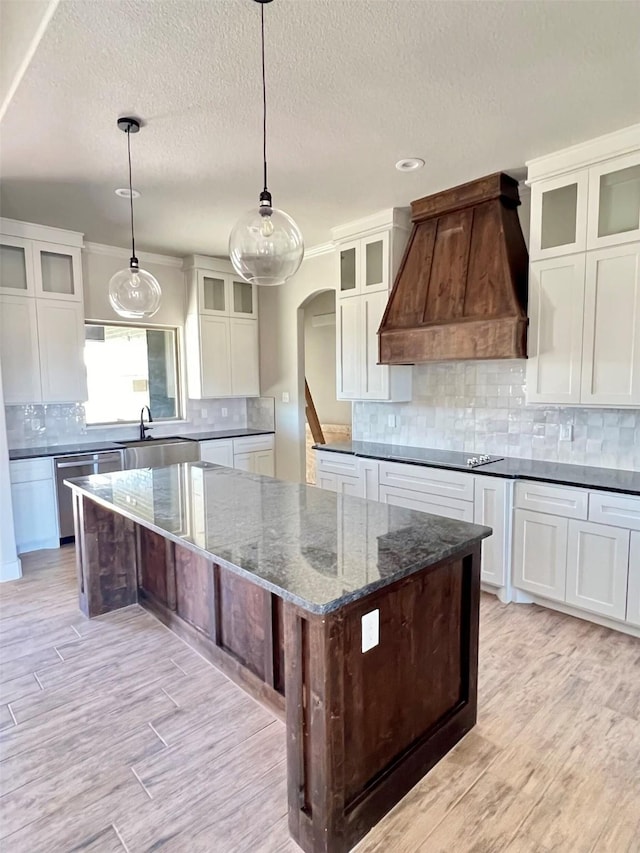 kitchen with decorative light fixtures, custom range hood, dark stone countertops, a spacious island, and stainless steel dishwasher