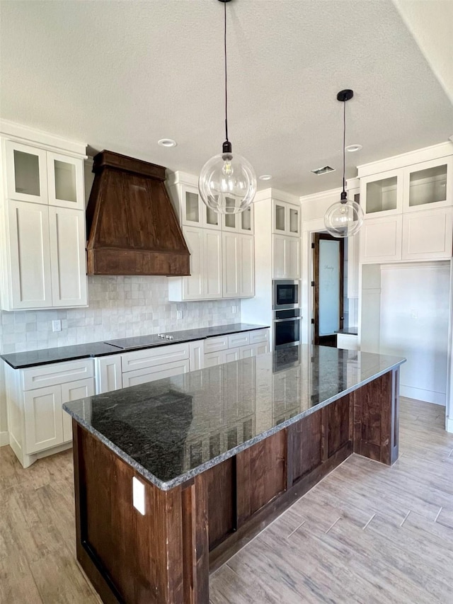 kitchen featuring white cabinets, pendant lighting, a spacious island, and custom range hood