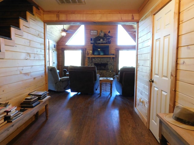 living room with ceiling fan, a stone fireplace, dark hardwood / wood-style flooring, lofted ceiling, and wooden walls