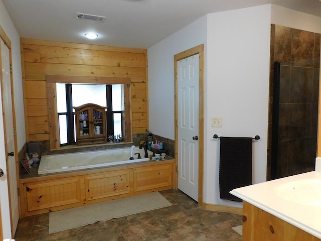 bathroom featuring a bathing tub, vanity, and wood walls