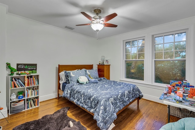 bedroom with ceiling fan, crown molding, a nursery area, and dark hardwood / wood-style floors