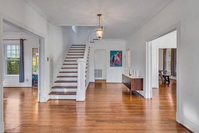 staircase featuring wood-type flooring, a notable chandelier, and ornamental molding