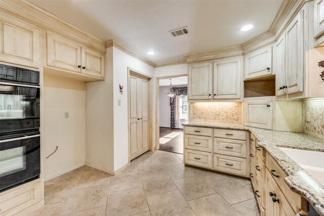 kitchen featuring backsplash, black double oven, light stone counters, and a notable chandelier