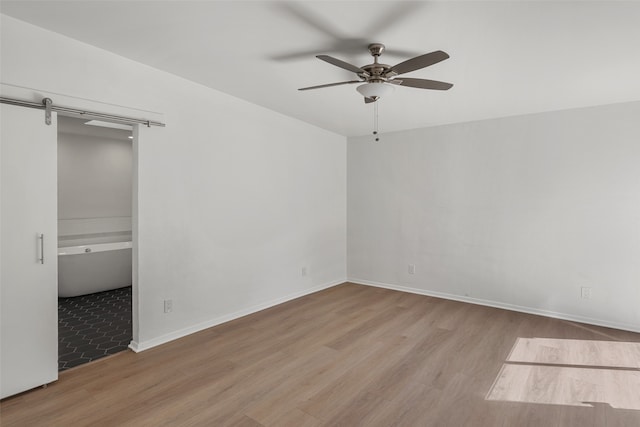 unfurnished bedroom with a barn door, ceiling fan, and light wood-type flooring