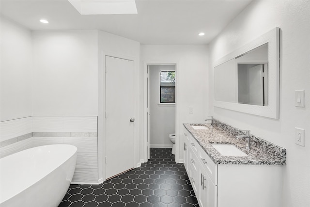 bathroom featuring a skylight, tile patterned flooring, toilet, a bathtub, and vanity