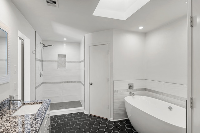 bathroom featuring plus walk in shower, vanity, a skylight, and tile patterned floors