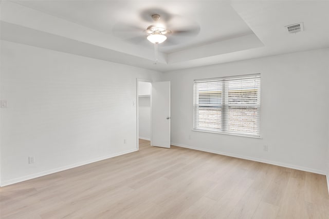 empty room with light wood-type flooring, a raised ceiling, and ceiling fan