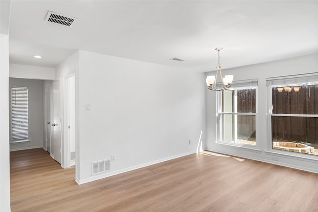 empty room with light hardwood / wood-style floors and an inviting chandelier