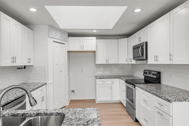 kitchen featuring sink, stainless steel appliances, light hardwood / wood-style floors, stone countertops, and white cabinets