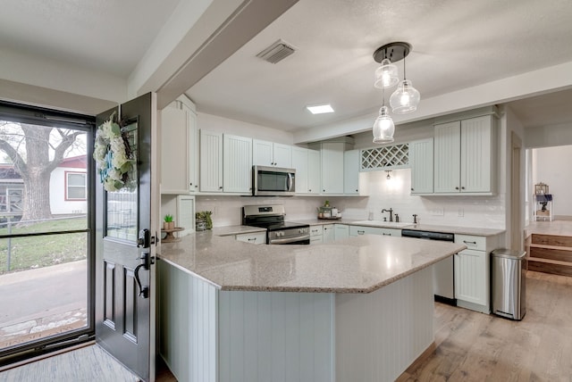 kitchen with kitchen peninsula, stainless steel appliances, sink, pendant lighting, and light hardwood / wood-style flooring